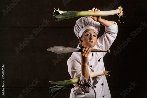 Sad clown chef with leeks and knife gazing at camera photo