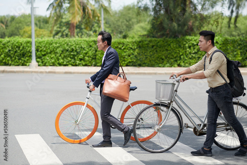 Determined Vietnamese businesssmen with bicycles crossing road in city when coming to work in morning