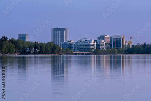 Modern financial district on the other side of a river. Tall buildings cast reflections on the calm water.