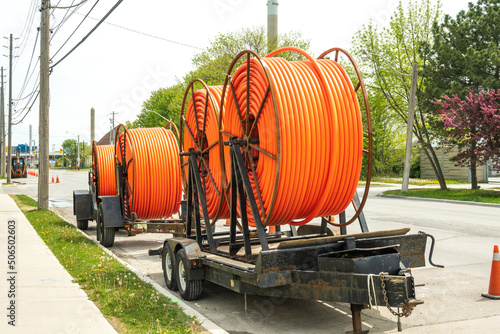 Large spools of smooth walled HDPE plastic cable (orange) conduit on trailers waiting to be installed and carry utility cables for new construction.  Shot in an industrial area of Toronto in spring.