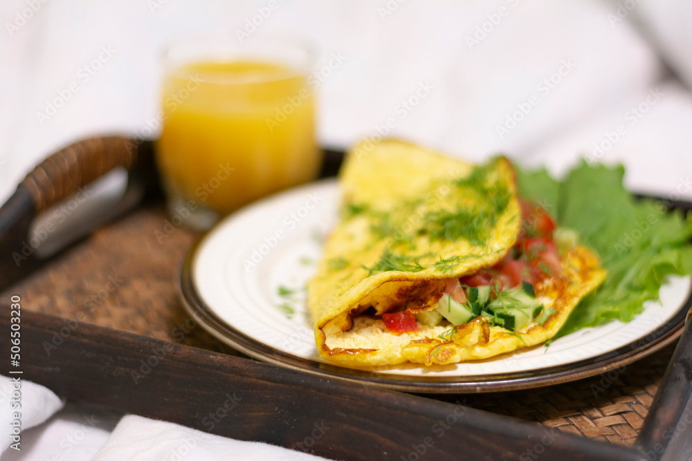 Close-up of a breakfast tray with scrambled eggs with herbs and a glass of orange juice in a stylish white bed no people. Concept: healthy breakfast in bed on a tray 