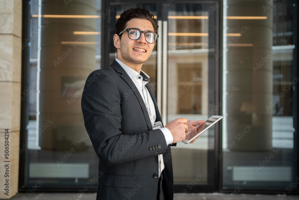Fototapeta premium Uses a tablet writes a message to a client a man in glasses and a formal suit a businessman