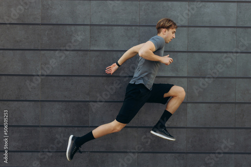 Full body side view of happy young sportsman running and jumping near black wall