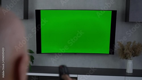 Elder man watching television turning on plasma flatscreen tv set and pointing remote control at empty screen on grey wall. photo