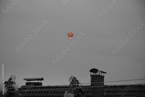 A view of a colorful ballon flying in the sky and being warmed up by means of a flame spotted on a cloudy yet warm summer day on a Polish countryside during a hike