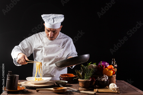 Male chef in white uniform prepares spaghetti with vegetables on the dish photo