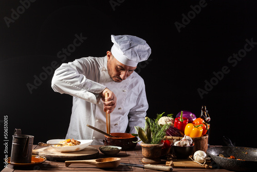 Male chef in white uniform prepares spaghetti with vegetables on the dish photo