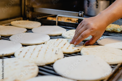 Colombian paisa arepa on a grill, local business. a lady's hand flips arepa photo