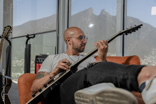 young bald man plays his electric guitar relaxing in a luxurious apartment with a mountain atrium.