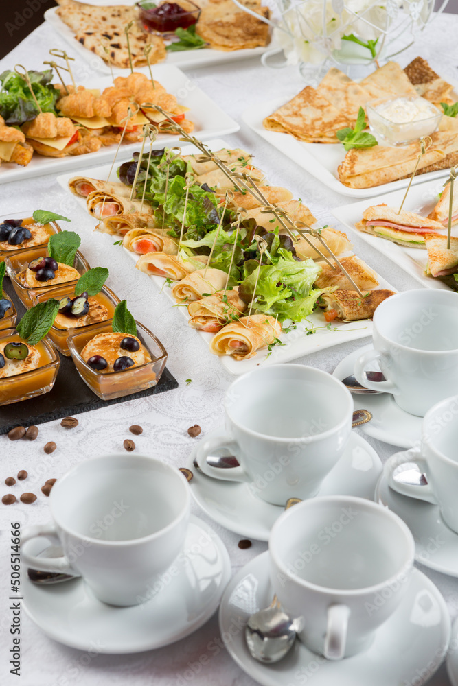 Festive buffet. An assortment of cold snacks on wooden crossbars and pancakes decorated with leaves of greens, jam and berries.