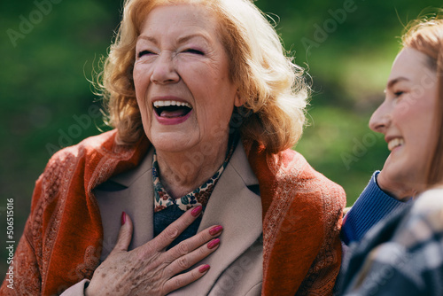 A grandmother is laughing and having fun with her adolescent granddaughter while sitting on the park bench.