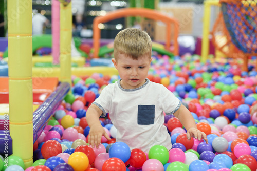 A boy in a dry paddling pool in playing centre with plastic balls.