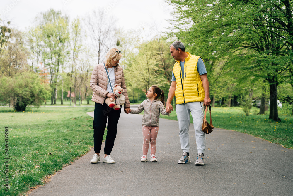 Cheerful little kid holding hands of grandparents in park Cheerful little kid holding hands of grandparents in park