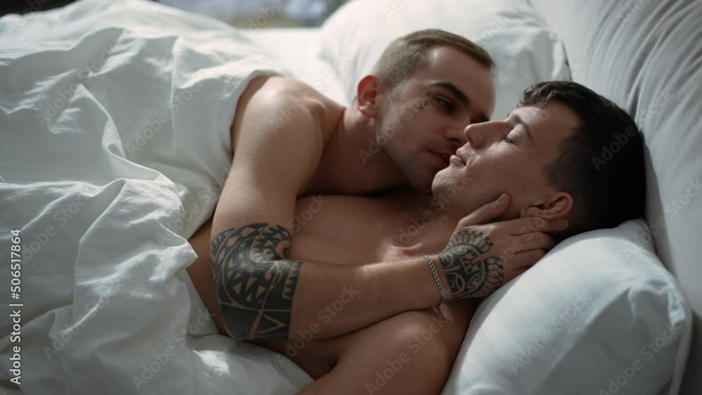 Side view young men sleeping in bed together waking up in the morning kissing cheek. Happy loving Caucasian gay couple in bedroom at home indoors. Leisure and love concept Side view young men sleeping in bed together waking up in the morning kissing cheek. Happy loving Caucasian gay couple in bedroom at home indoors. Leisure and love concept