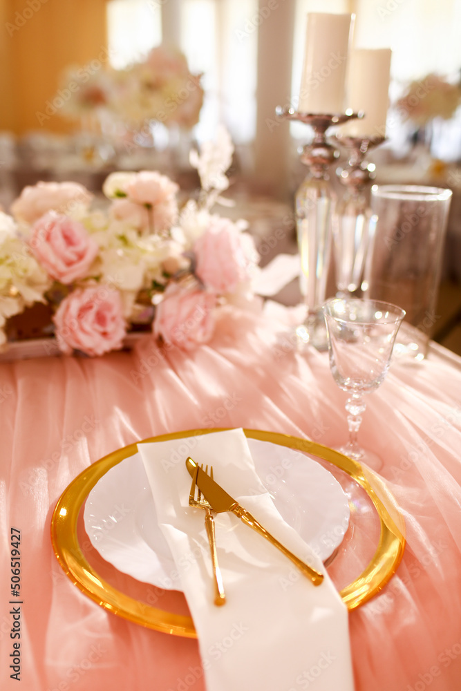 table decoration with pink tablecloth, crystal candlesticks with candles and white pink flowers in restaurant . stylish wedding day. setting table with gold plate, fork and knife