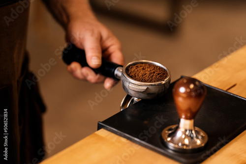 Crop anonymous man using tamper for pressing ground coffee in portafilter