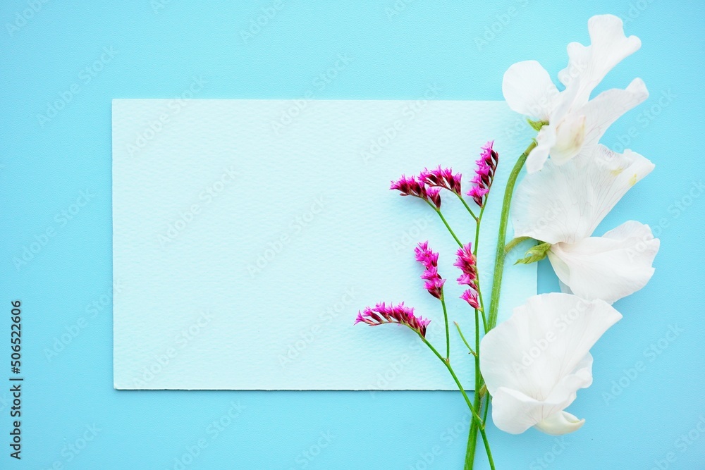 Naklejka premium 青バックに白いスイートピーと赤紫色のスターチスを添えたかわいいタイトルカードのモックアップ