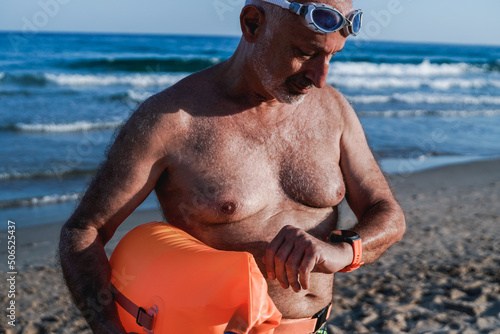 Sport senior man using smart watch after open water swimming routine at the beach - Elderly healthy lifestyle photo