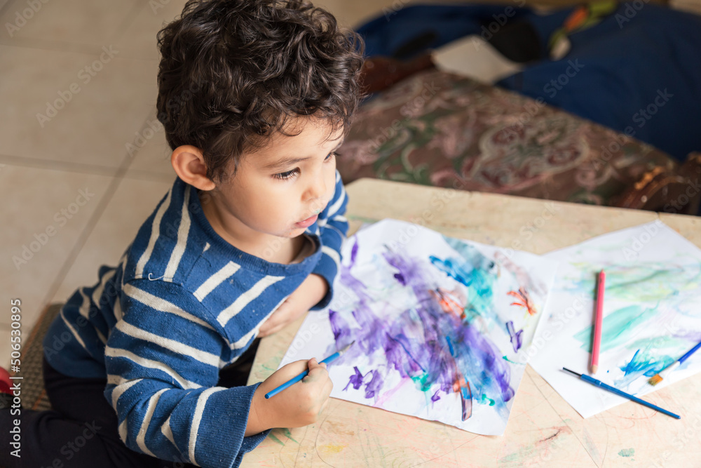 child painting with paints and colored pencil making a drawing