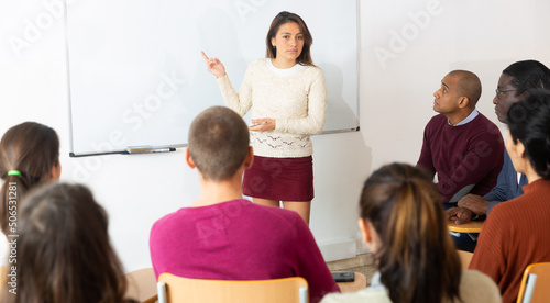 Group of students attentively listening to lecture of female teacher in classroom