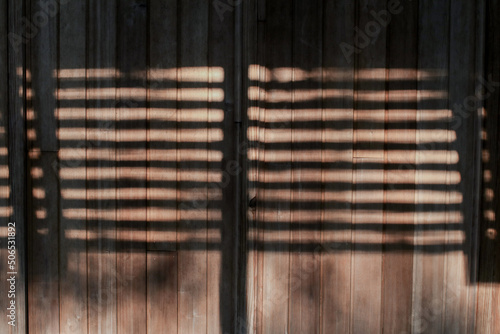 Shadows and sunlight on a brown wooden wall. Beams of sunlight through old window wooden blinds.