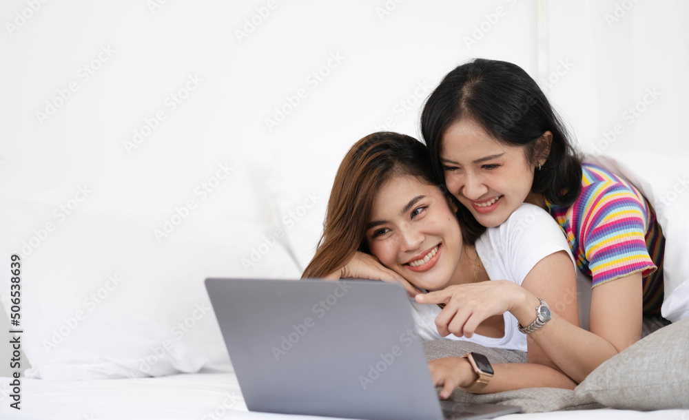 A couple of lovely woman listening song and watch movie with laptop   in bed while smiling. They are happiness and building good relationships in the future.