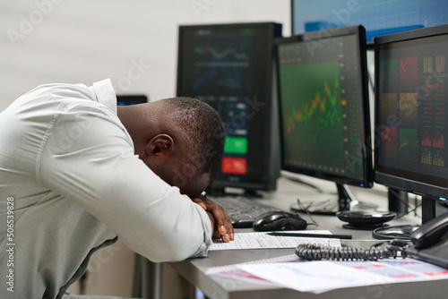 Exhausted young African American man working in brokerage agency having burnout laying his head on desk
