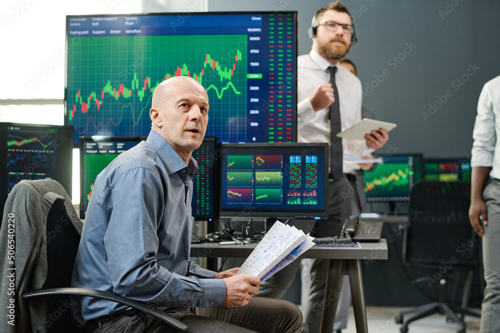 Group of professional investment specialist waiting for current stock trading finish looking at monitor in office Group of professional investment specialist waiting for current stock trading finish looking at monitor in office