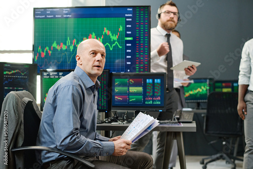 Group of professional investment specialist waiting for current stock trading finish looking at monitor in office