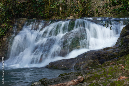 The jets of the waterfall flow into a mountain river flowing over rocks in the middle of a tropical forest.