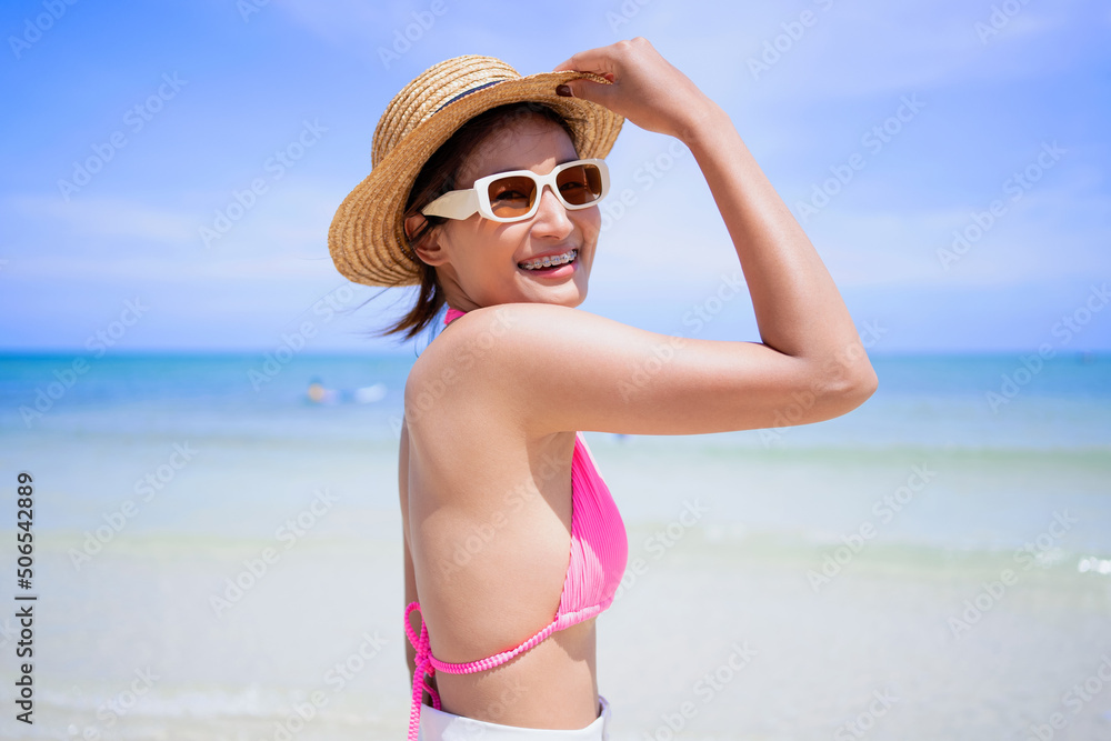 Cheerful young woman in pink bikini at beach. Happy smiling girl enjoying the beach and looking at camera. Asia tanned woman feeling refreshed  during summer vacation.