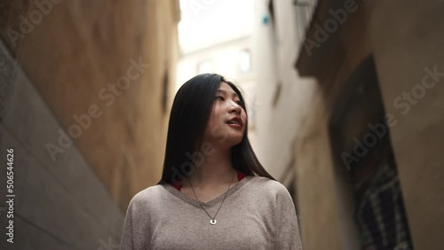Conceptual shot of long haired Asian woman walking down the cozy narrow street. Pretty Pretty brunette girl exploring new places