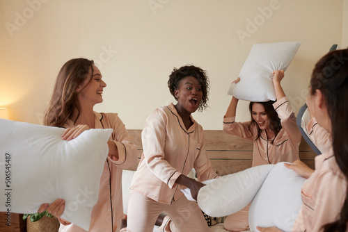 Group of excited young women in pajamas having pillow fight at sleepover party photo