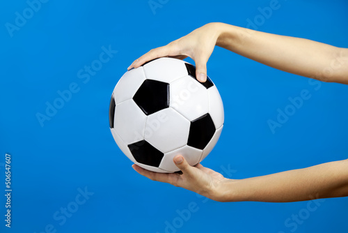 female hand holding soccer ball isolated blue wall background, spaort concept © CREATIVE WONDER