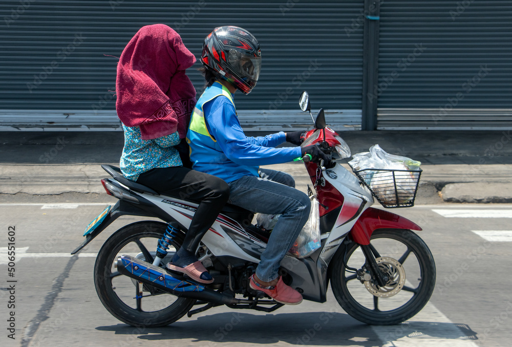 A motorcycle taxi rides on the street with a woman hidden under a towel A motorcycle taxi rides on the street with a woman hidden under a towel