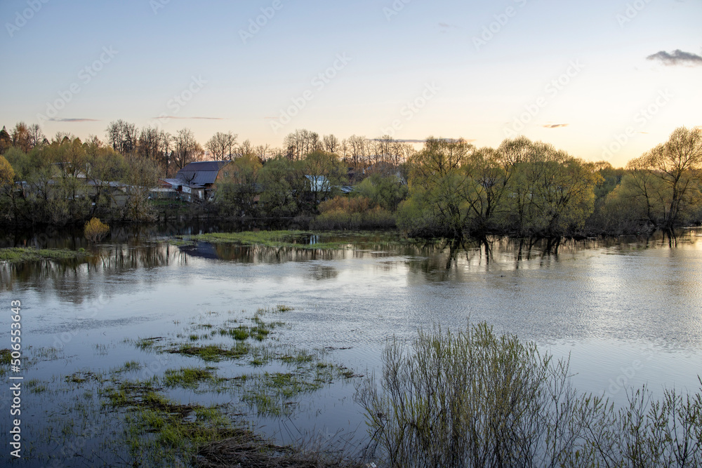 Evening in early spring in May. The river overflowed its banks and flooded the houses. Rural landscape with a river at sunset.