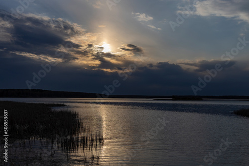 Evening dramatic landscape  lake in spring  sun shining through blue clouds. Ripples on the water from a strong wind.