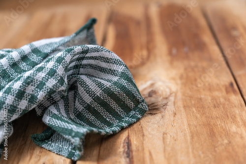 Fototapeta Naklejka Na Ścianę i Meble -  A green checkered kitchen towel lies on the countertop of a wooden table. Crumpled Towel or kitchen napkin on rough boards. Selective Focus.