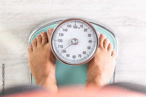 Woman looks down at the number of pounds or kilograms as she stands on a weighing scale