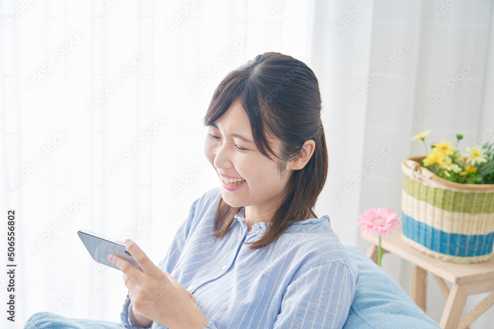 リビングでスマホを見て笑う女性