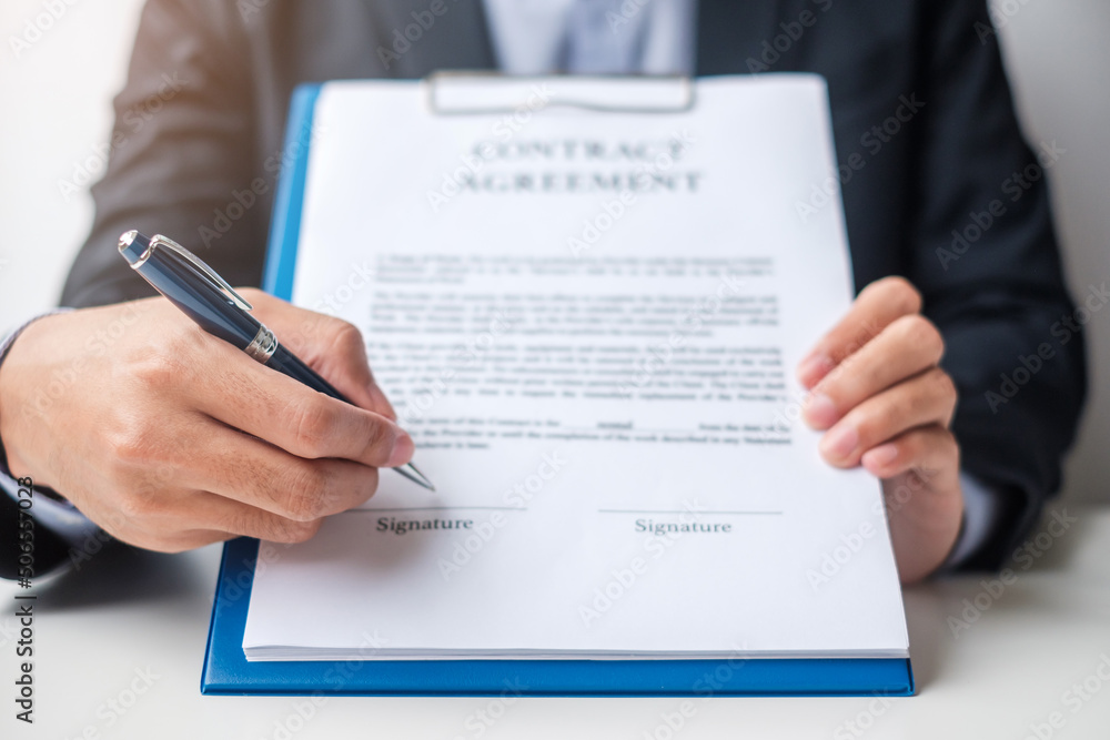 Businessman signing on contract documents after reading, man holding pen and approve on business report. Contract agreement, partnership and deal concepts Businessman signing on contract documents after reading, man holding pen and approve on business report. Contract agreement, partnership and deal concepts