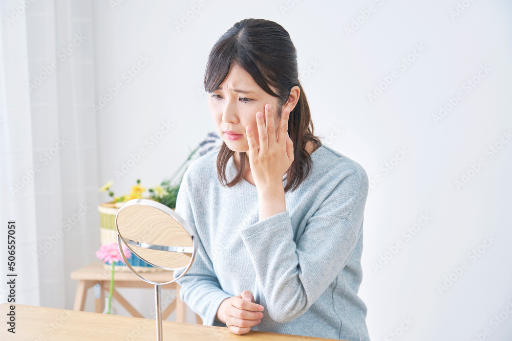 リビングで鏡で顔を見て困っている女性 リビングで鏡で顔を見て困っている女性