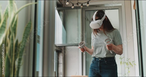 Young woman moving hands wearing virtual reality goggles and control handles