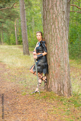 medieval cutthroat woman wearing leather plastron, bracer, shoulder guard and skirt  with morglay in her hands keeps watch and ward on the road in the wood photo