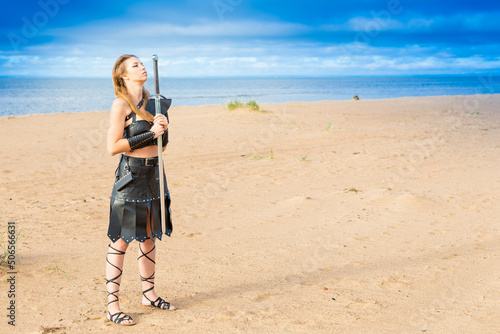 medieval Viking cosplayer wearing leather plastron, skirt, bracelets and rerebrace with two-handed falchion is standing at the sandy beach photo