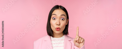 Close up portrait of businesswoman raising finger up, suggesting, got an idea or solution, standing over pink background