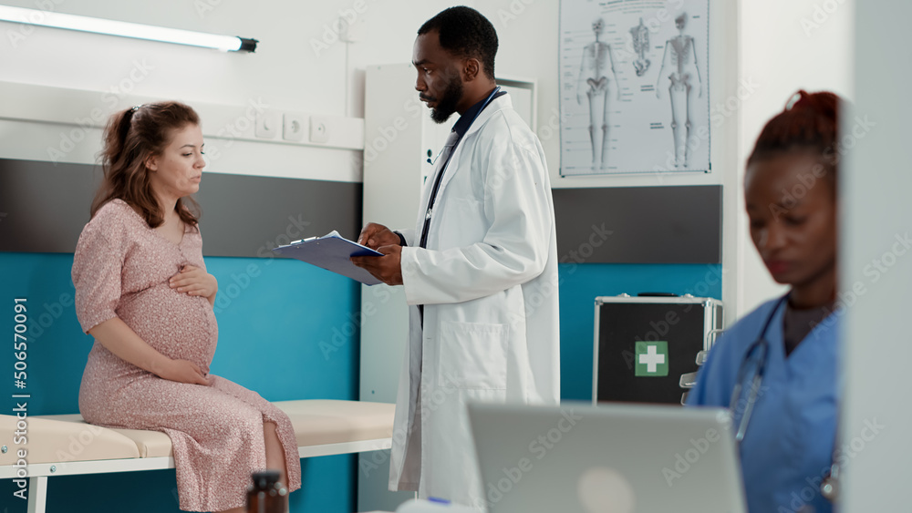 Obraz premium General practitioner doing pregnancy consultation with future mother, helping with childbirth. Health specialist talking to woman expecting child in medical office, checkup visit.