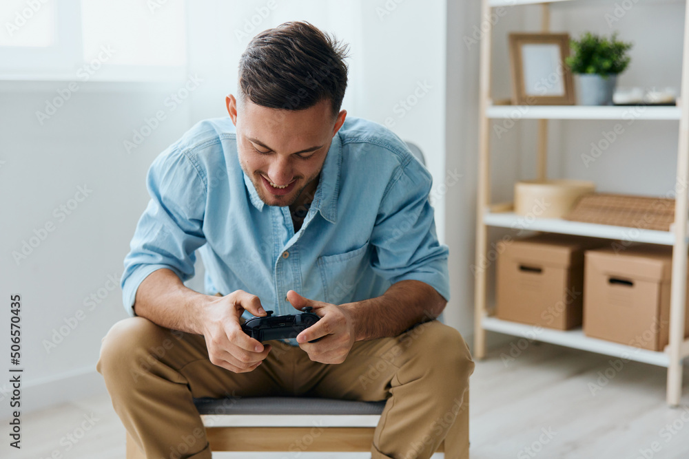 Crazy irritated young tanned gamer looks at joystick gamepad trying win at home interior. Player Stream Platform for gamers concept. Relaxing Active recreation. Copy space for game console advertising