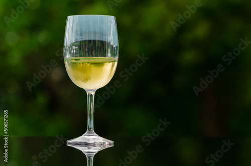 A glass of white wine put on table with dark green background.