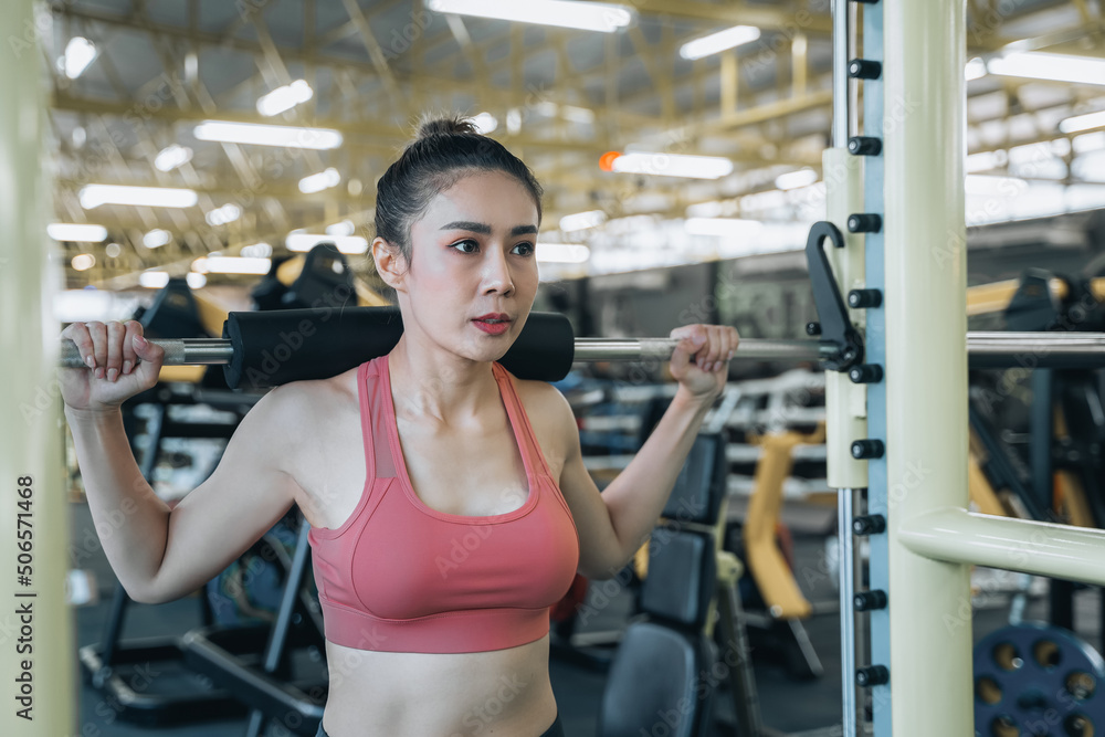 Fototapeta premium Young woman bodybuilder with barbell flexing muscles doing squats in gym. Concept of sports, gyms, fitness, bodybuilding. Preparing for the competition.